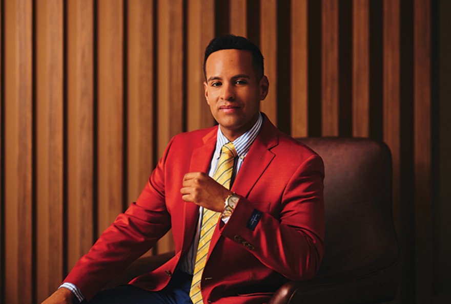 Andrew Goldstein seated in a wood-panelled room, wearing a red jacket and striped tie